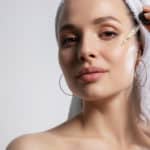 woman in bath towel on head applying oil serum