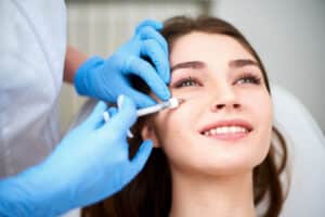 A woman smiling while getting a dermal filler injection in her cheek