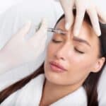 Woman with braids receives a Botox injection between her brows to minimize her frown lines