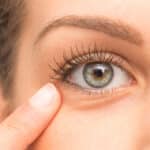 A close-up shot of a woman pointing to her under-eye hollows