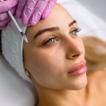 Close-up of a young cosmetologist administering preventative Botox® injections to a relaxed female patient, helping to reduce fine lines and delay wrinkles.